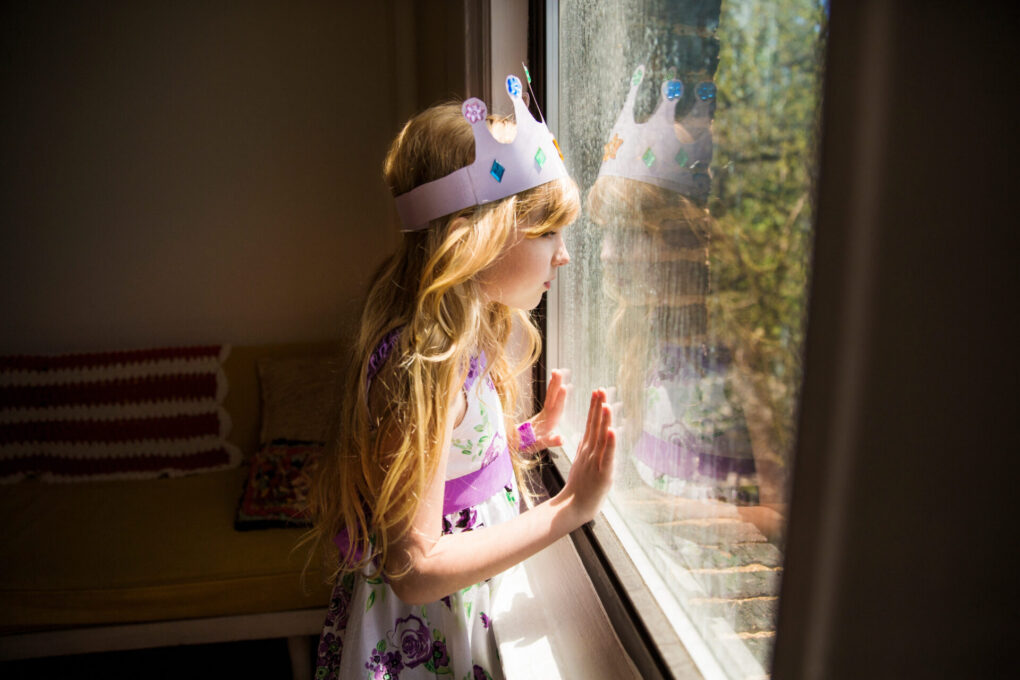 Side view of girl looking away while standing by window at home