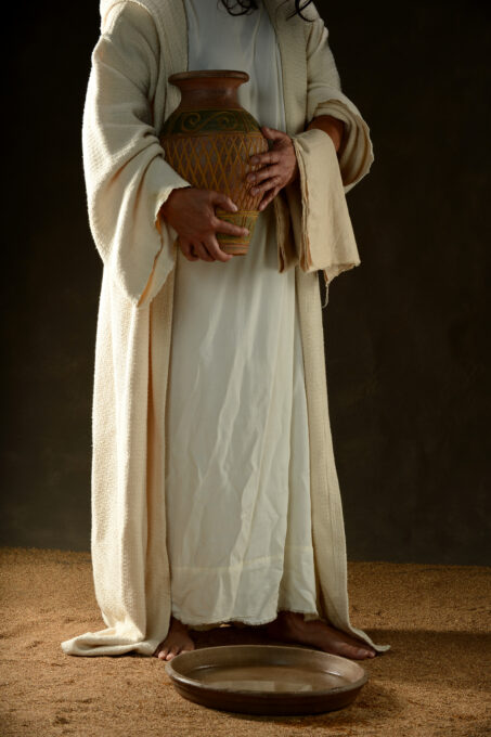 Jesus holding a jar of water standing up with a dark background