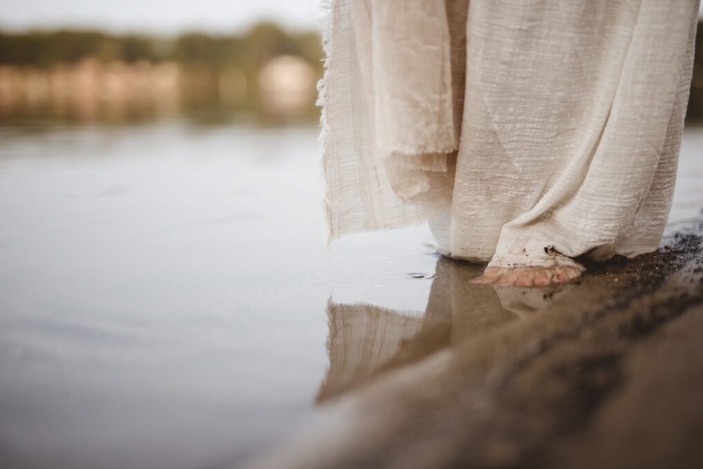 A closeup shot of a person wearing a biblical robe walking on the shoreline