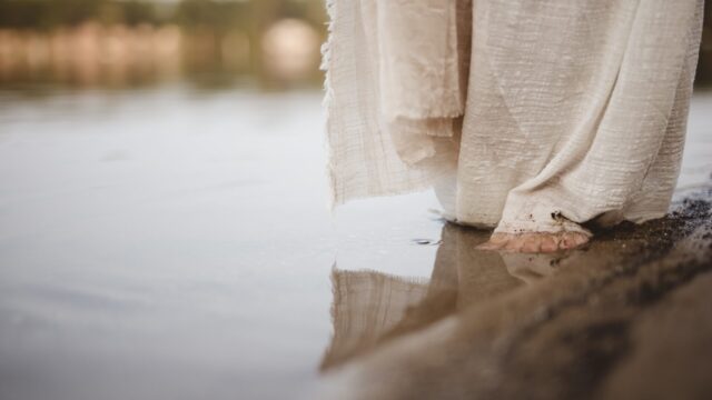 A closeup shot of a person wearing a biblical robe walking on the shoreline