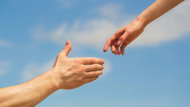 Giving a helping hand. Hands of man and woman on blue sky background. Lending a helping hand. Solidarity, compassion, and charity, rescue. Hands of man and woman reaching to each other, support.